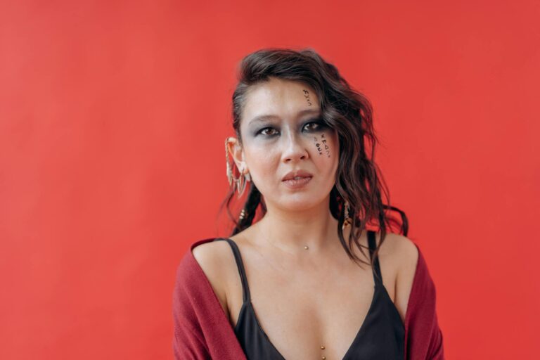Artistic portrait of a young woman with styled hair and makeup, set against a vibrant red backdrop.