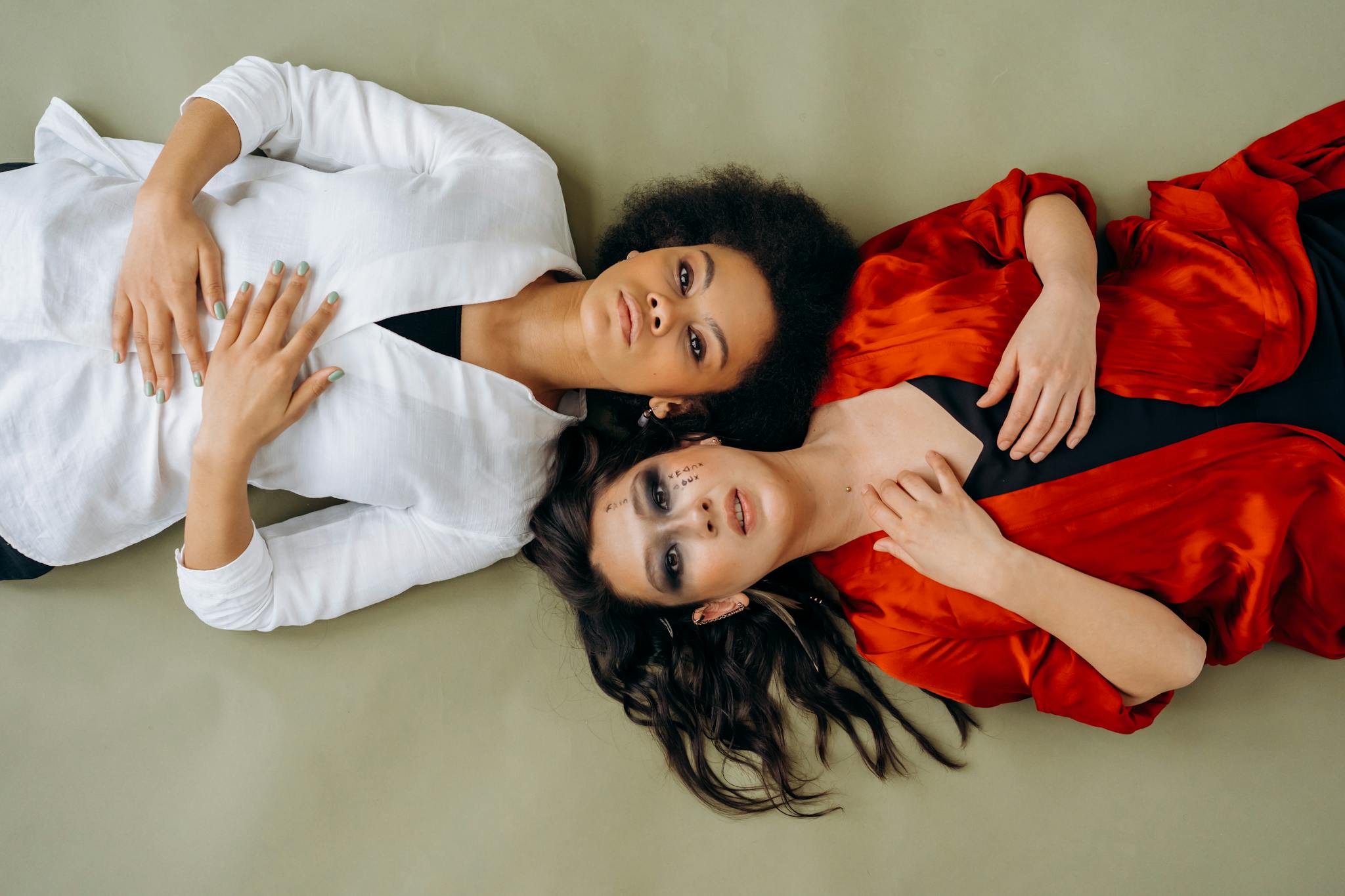 Two women in stylish outfits lying on the floor, expressing elegance and poise.